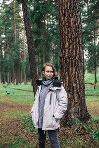 Smiling young woman looking away while standing against tree trunk in forest