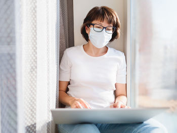 Woman in medical mask works remotely from home with laptop. lockdown quarantine , coronavirus.