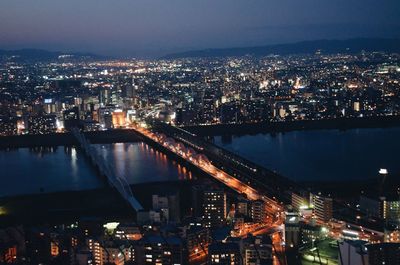 Illuminated cityscape by river against sky at night