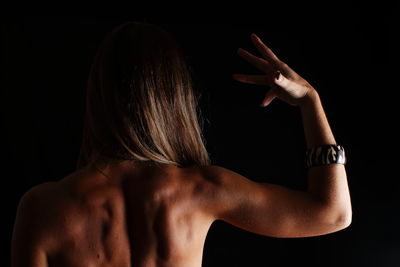 Rear view of shirtless young woman against black background