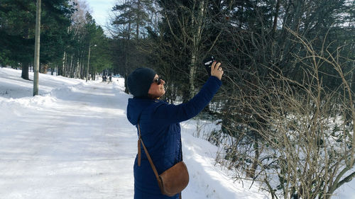 Man photographing while standing on snow covered tree