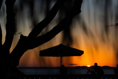 Silhouette people standing by sea during sunset