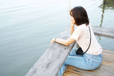 Woman sitting on pier by lake
