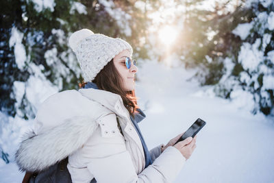 Woman at sunset in snowy mountain using mobile phone. nature and technology concept. winter season