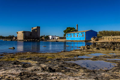 Buildings by sea against clear blue sky