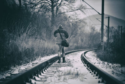 Rear view of man walking on railroad track in winter