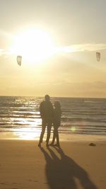 Silhouette friends standing on beach against sky during sunset