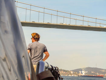 Rear view of man standing by bridge over river against sky