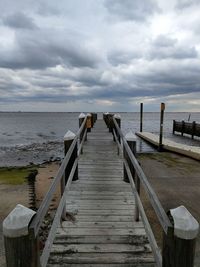 Wooden jetty leading to pier over sea against sky