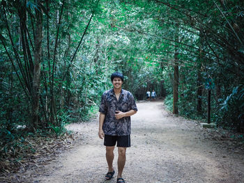 Full length portrait of young man standing on road in forest