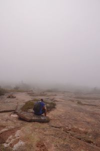 Man sitting on land against sky