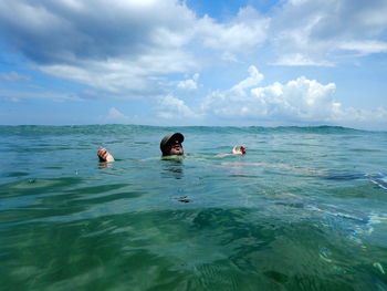 Man swimming in sea against cloudy sky