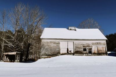 Snow covered field by building against sky