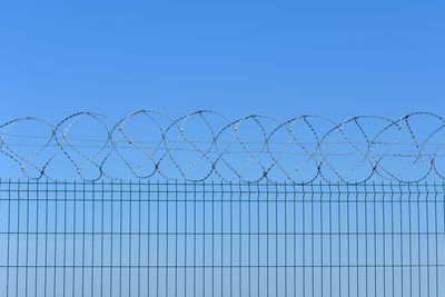 Barbed wire fence against clear blue sky