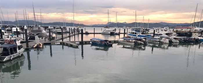 Boats moored in harbor at sunset
