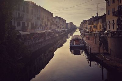 Boats moored on canal in city against sky