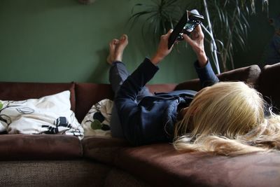 Woman using mobile phone while relaxing on sofa