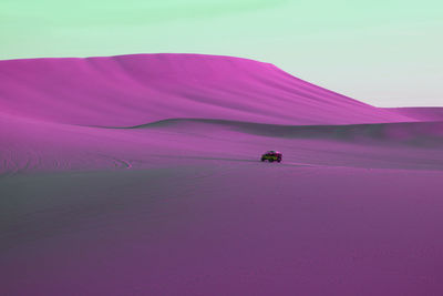 Surreal style vivid purple pink colored desert with a running dune buggy under pastel green sky