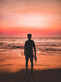 Rear view of man standing on beach during sunset