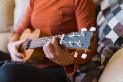 Midsection of woman playing ukulele at home