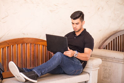 Portrait of young man using laptop on bench