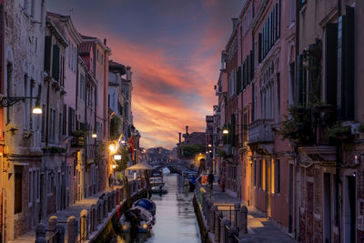 Narrow street amidst buildings against sky at dusk