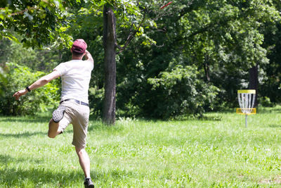 Full length rear view of man skateboarding on grass against trees