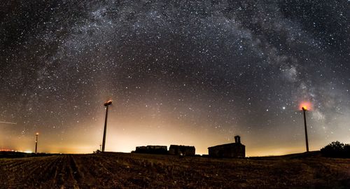 Low angle view of ruins among windmills on field against sky and milkyway at night 