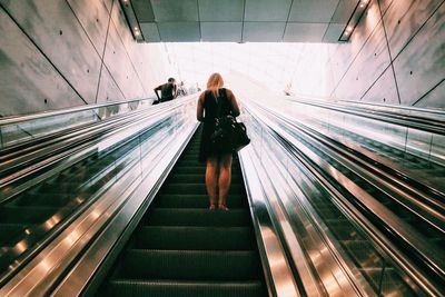 Rear view of woman moving up on escalator