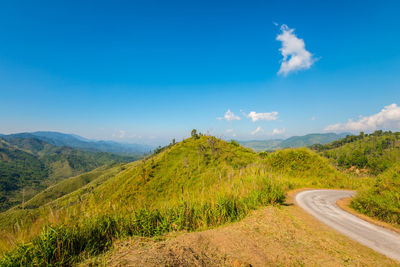 Road amidst green landscape against blue sky