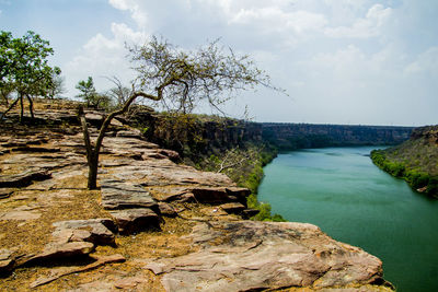 Scenic view of rocks by trees against sky