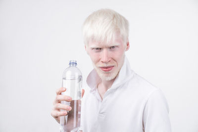 Portrait of man with albino holding water bottle against white background