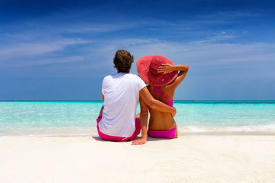 Rear view of couple sitting at beach against sky