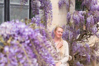 Beautiful middle-aged woman sits on a bench in the thickets of blooming wisteria