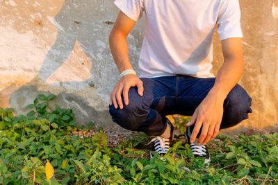 Low section of man crouching on grass against wall