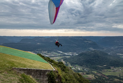 Rear view of person paragliding over landscape against sky