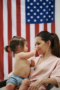 A young woman sitting with her daughter with the american flag in the background. 