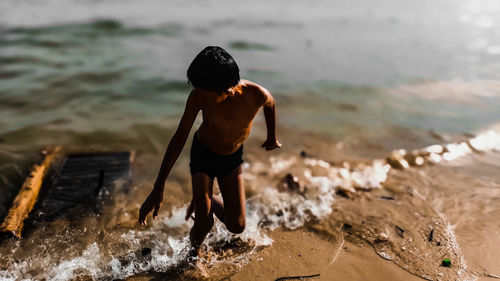 Rear view of shirtless boy standing on beach