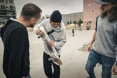 Male friends looking at skateboard while standing at park