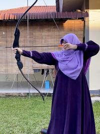 Full length of woman standing on field doing archery
