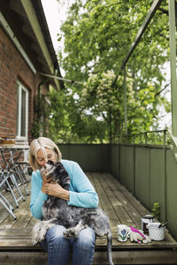 Happy senior woman kissing dog while sitting on porch
