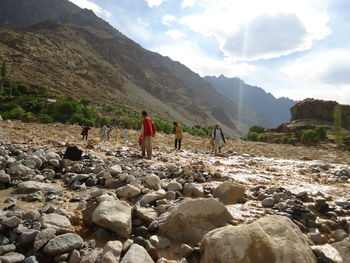 People on rocks by mountains against sky