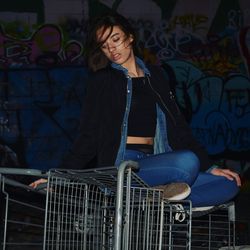 Young woman sitting on cart against graffiti wall at night