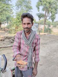 Portrait of smiling young man having food against plants