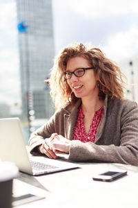 Portrait of a smiling young woman using phone on table