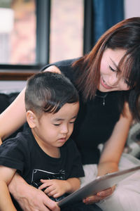 Woman showing digital tablet to son while sitting on bed at home