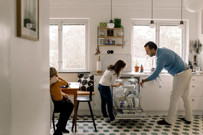 Father and daughter arranging utensils in dishwasher while standing at kitchen