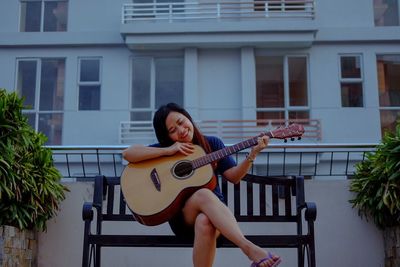 Young woman playing guitar against building