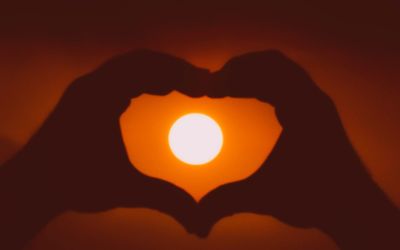 Close-up of hand holding heart shape against orange sky