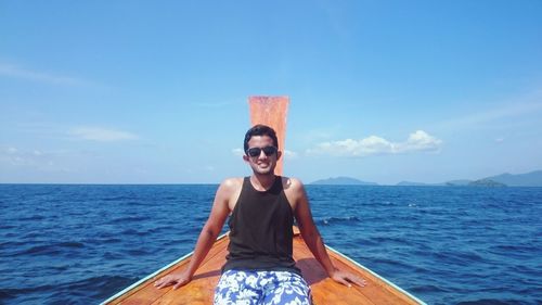 Portrait of young man sitting in boat on sea against sky